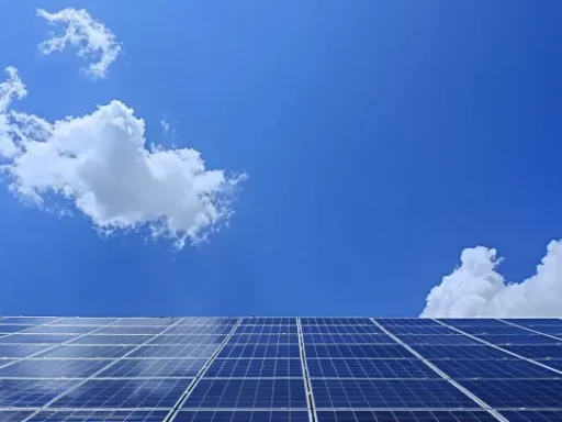 En stor samling av blå solpaneler ses under en klar himmel med några vita moln som reflekterar solljus. Kompositionen betonar förnybar energi och ren teknik, vilket skingra vanliga myter om solenergi med solpanelerna framträdande mot den livfulla blå bakgrunden.